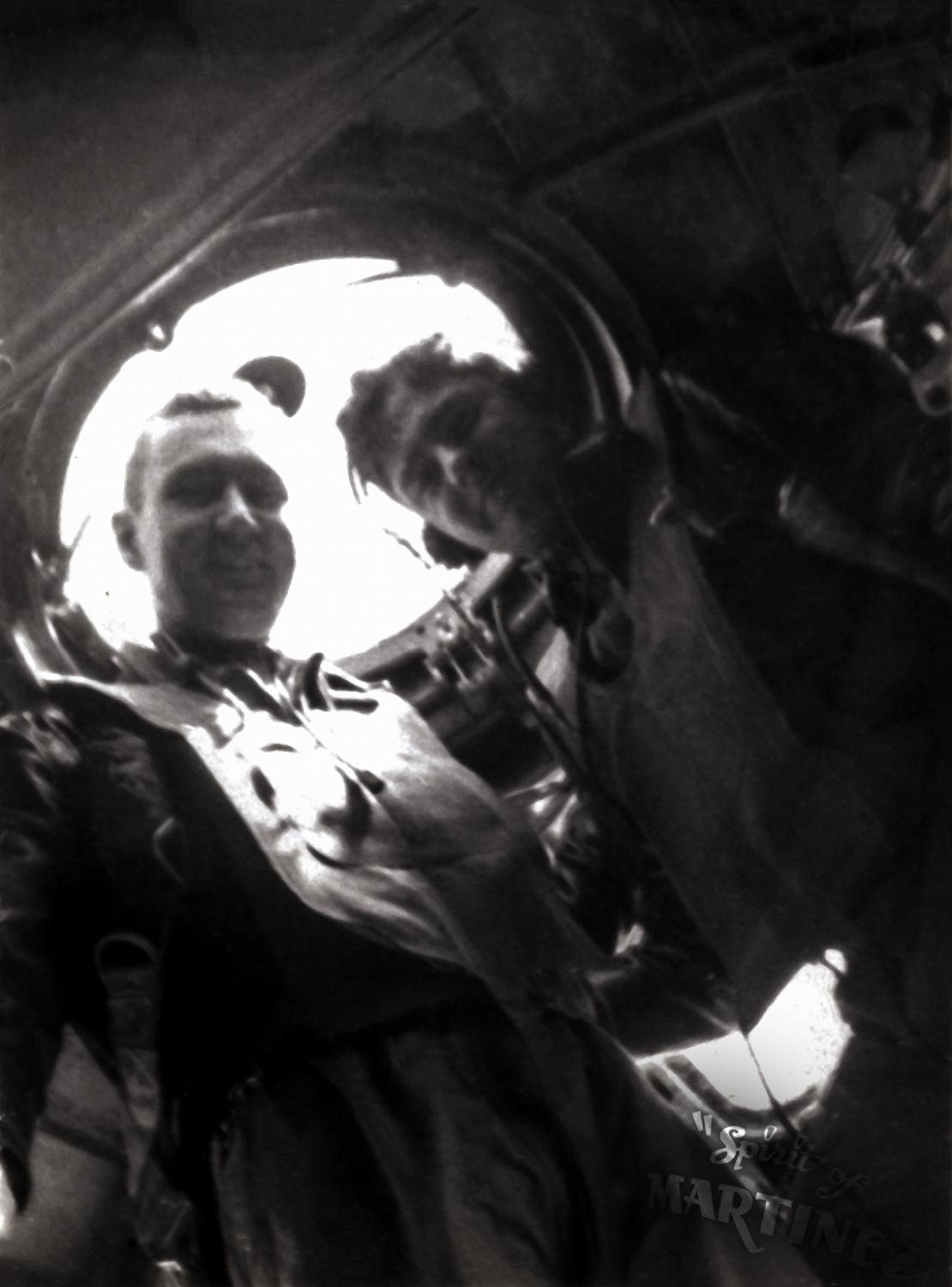 Navigator John R. Barnes at a B-17 window, backlit, another airman behind him