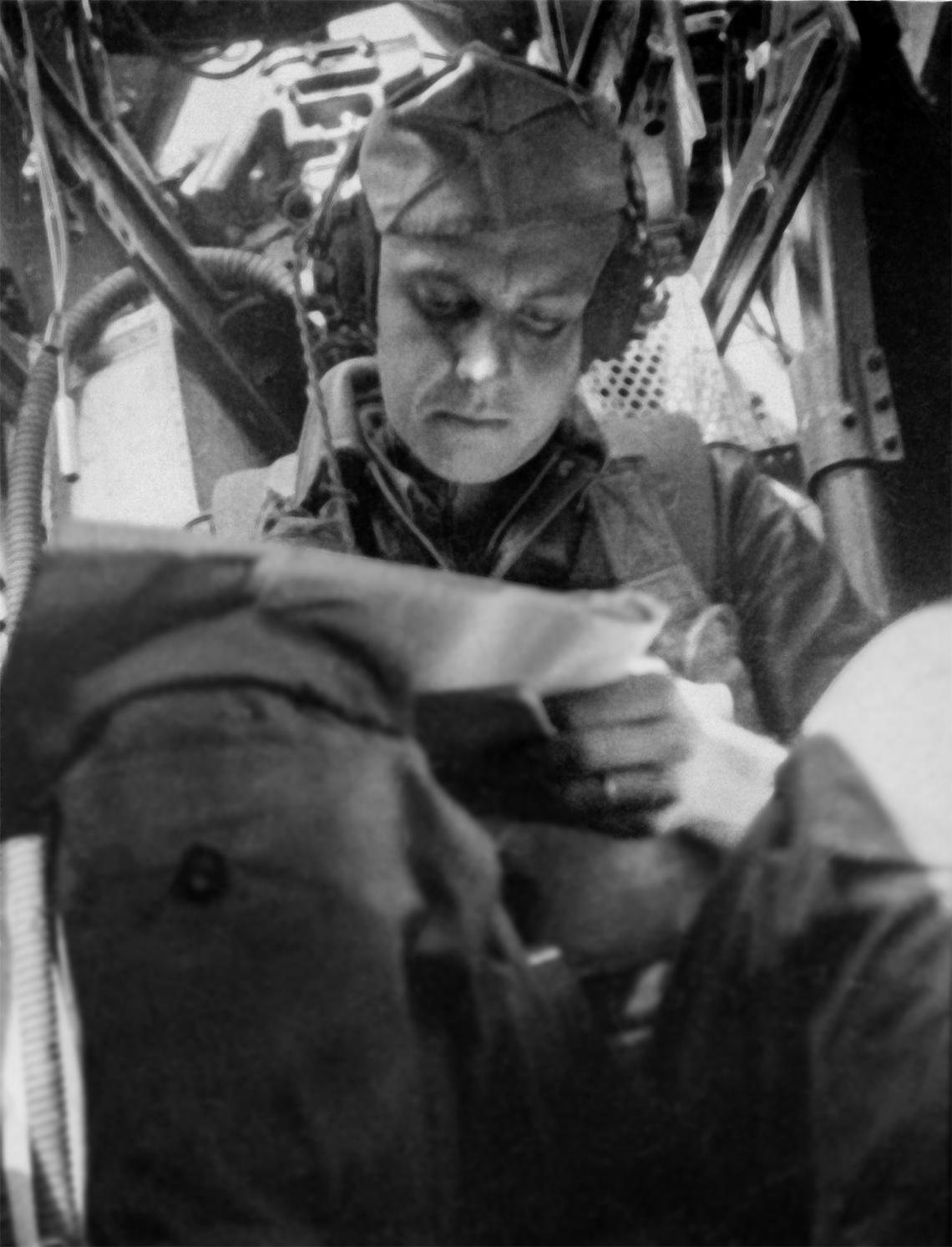Flight engineer Earle F. Bogacki in a B-17, looking down at a chart, a hatch open above him