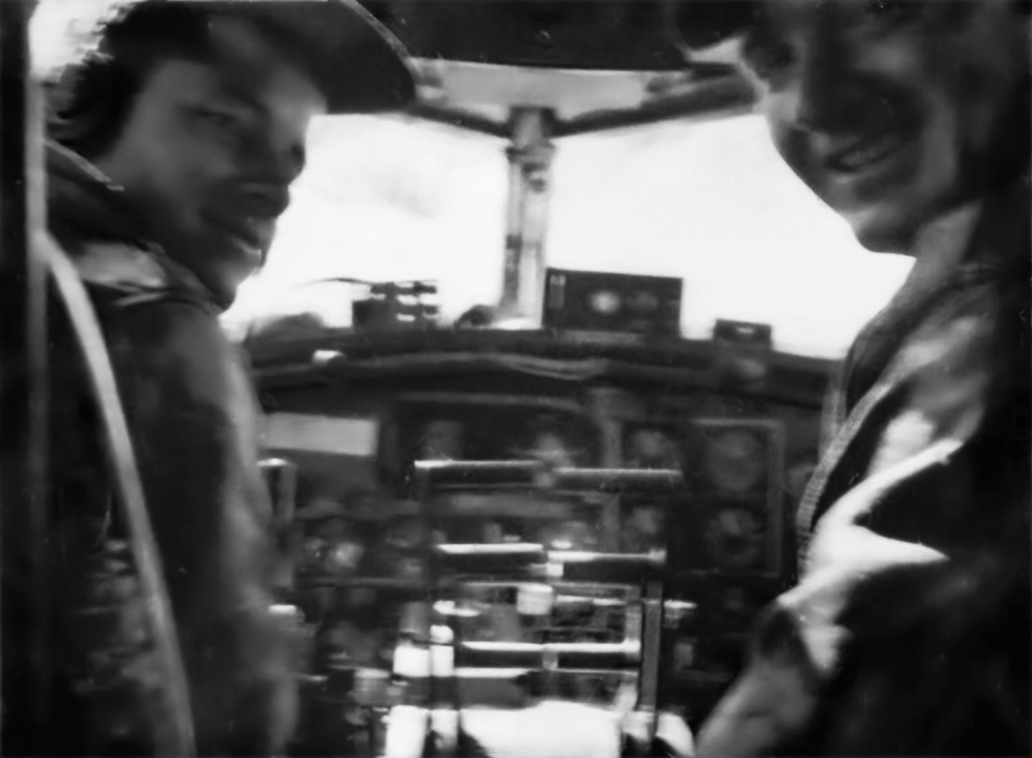 Frank Calicura and Victor Probst looking back from the seats of a B-17 cockpit, the instrument panel between them