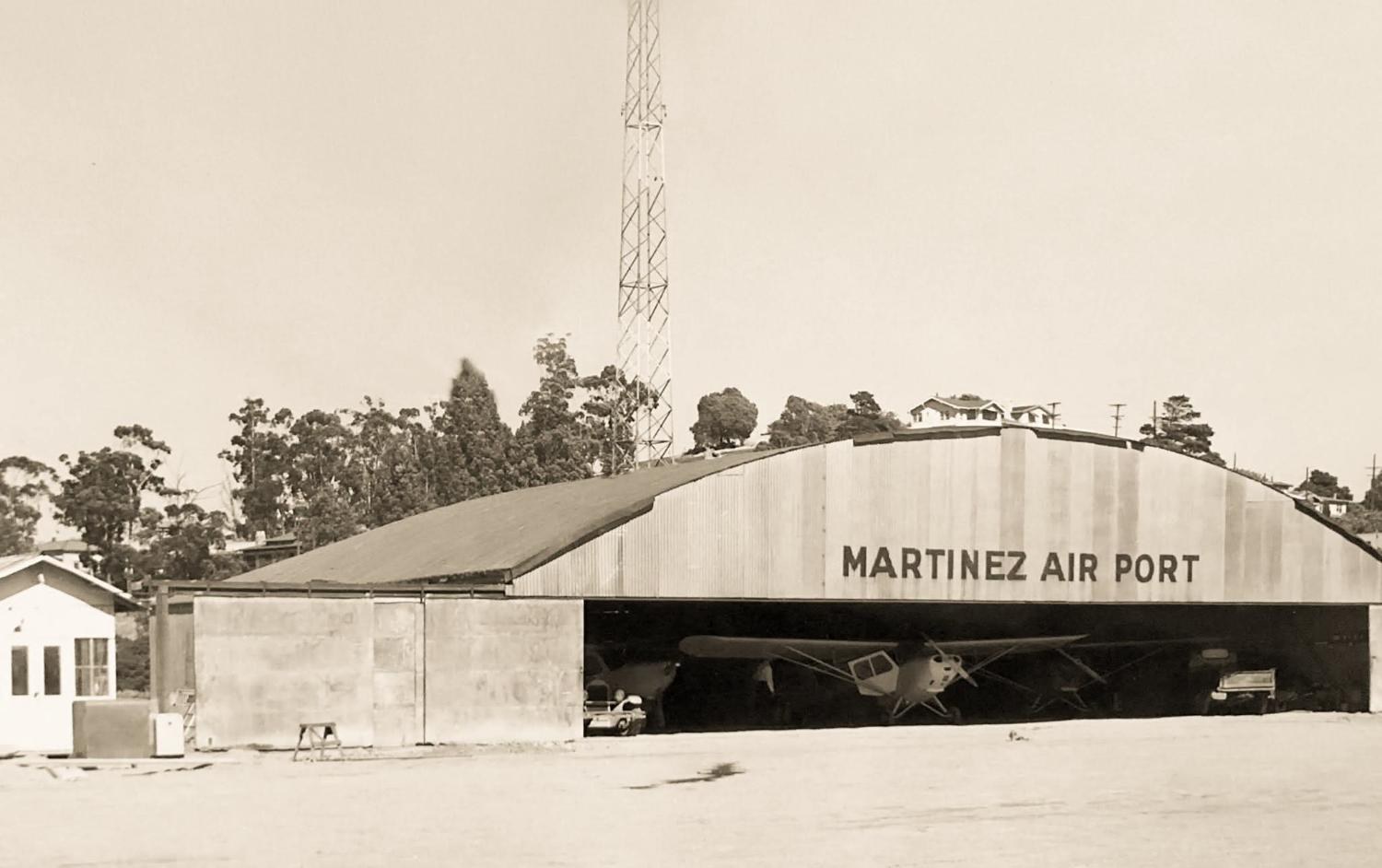 Corrugated hangar lettered MARTINEZ AIR PORT, light aircraft parked inside, a radio mast behind, a small office at left