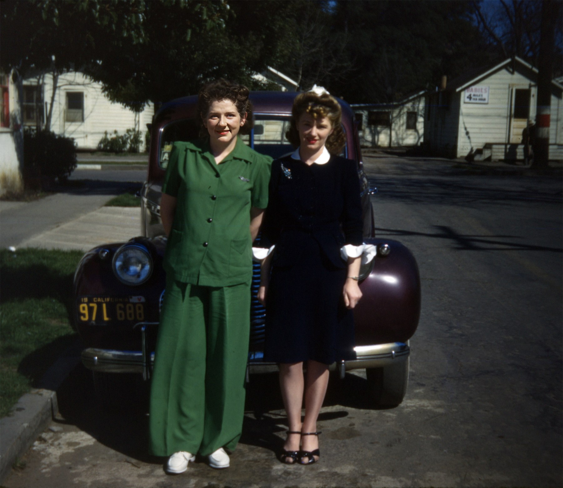 Joyce Calicura in a green suit standing with another woman in navy in front of a maroon car, California plate 97 L 688