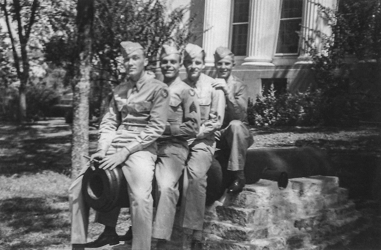 Four aviation cadets in khaki sitting on a gun in front of a columned building