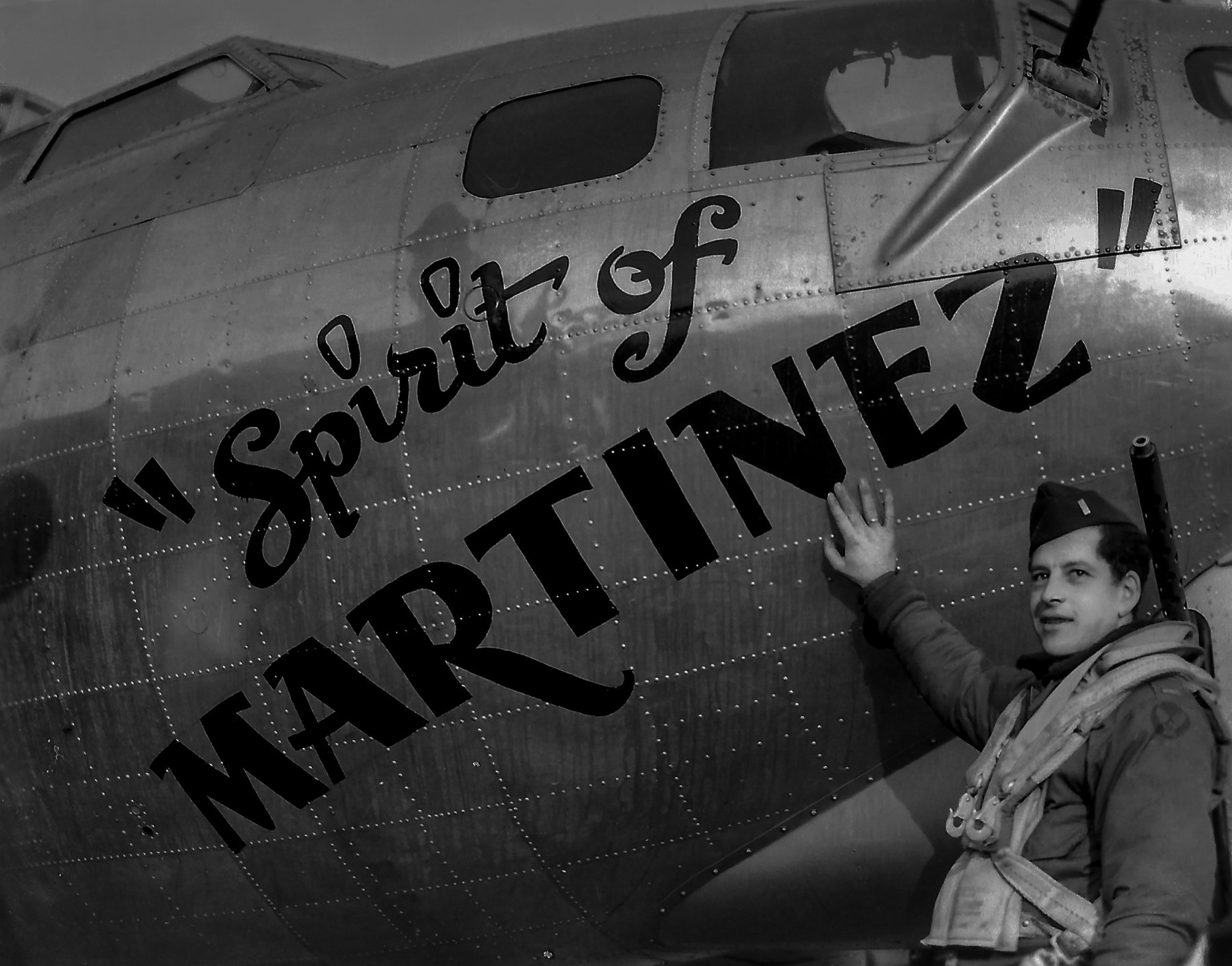 Frank Calicura in flying kit standing at the painted nose of a B-17, his hand on the word MARTINEZ