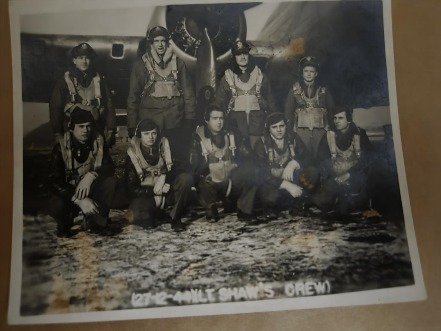 Nine airmen in flying kit posed in two rows under a B-17, the print labeled 27-2-44 Lt. Shaw’s Crew